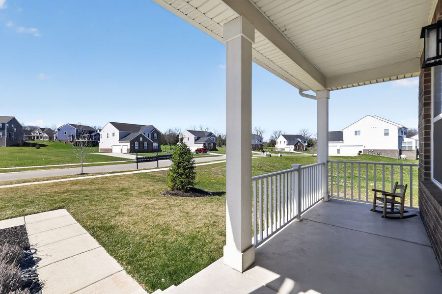 Spacious covered front porch with white railings overlooking a green lawn and suburban neighborhood on a sunny day.