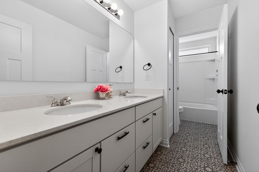 Modern bathroom with double white vanity, quartz countertop, large mirror, patterned tile floor, and shower-tub combo.