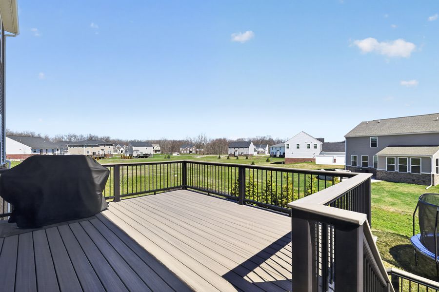 Spacious outdoor deck with black railing, gas grill, and suburban neighborhood views.