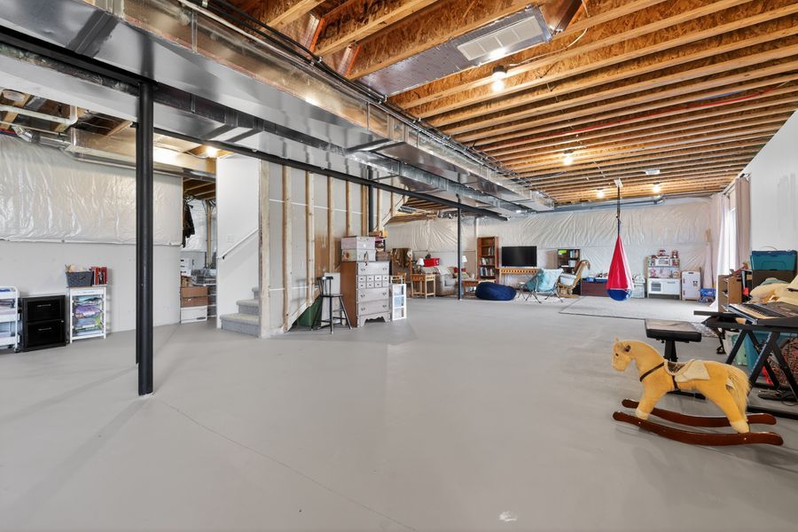 Spacious unfinished basement with exposed beam ceiling, gray concrete floors, and open layout perfect for storage or recreation.