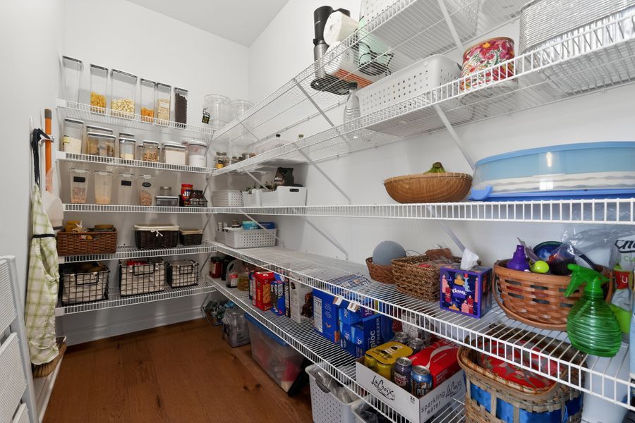 Well-organized pantry with white wire shelving stocked with food, baskets, and household supplies on hardwood floors.