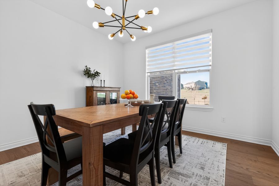 Bright dining room with wooden table, black chairs, modern chandelier, and large window on hardwood floors.
