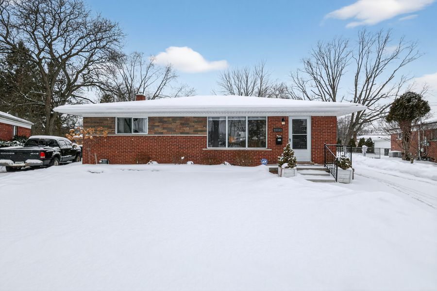 Brick ranch-style home exterior covered in snow with a wide front yard and mature trees in winter.