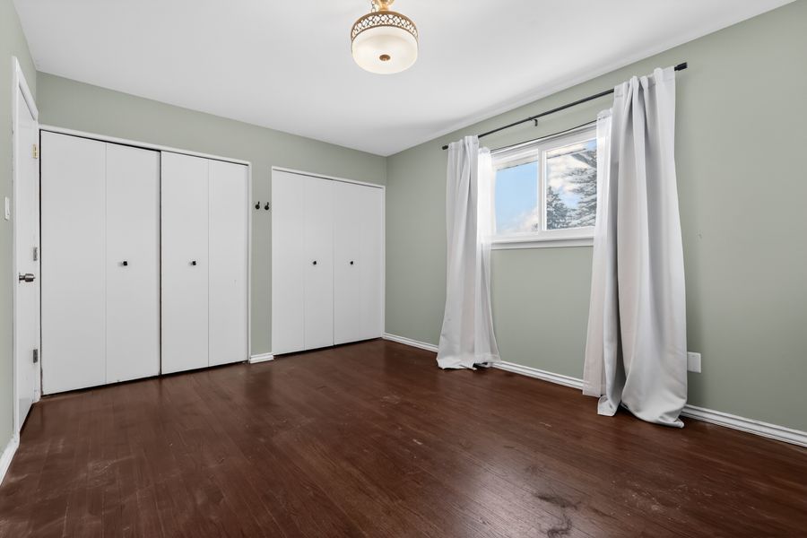 Spacious bedroom with dark hardwood floors, sage green walls, two white closets, and a bright window with white curtains.