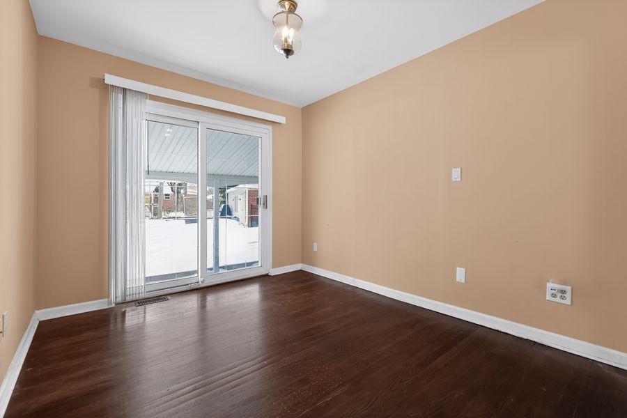 Empty room with dark hardwood floors, peach walls, sliding glass door, and white baseboards in a residential home.