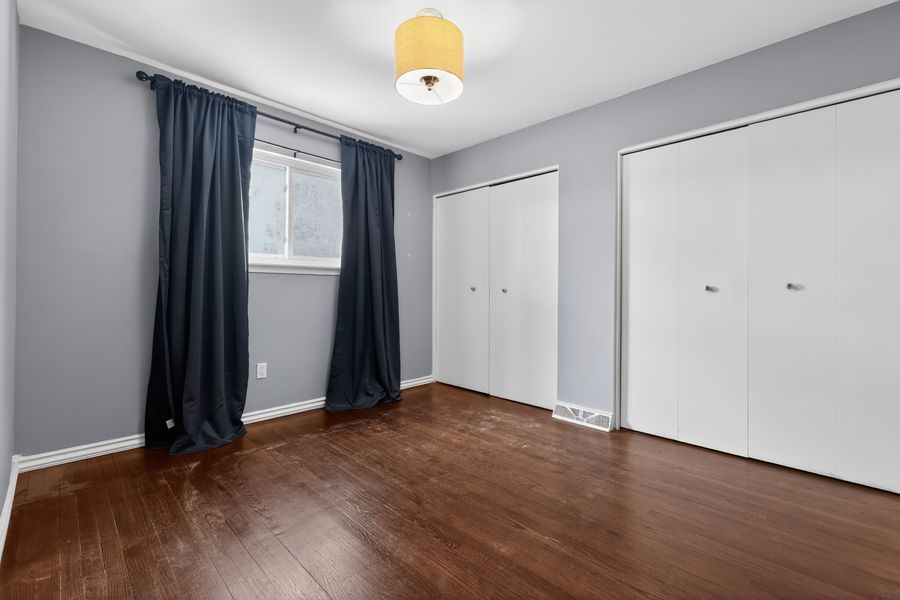 Bright bedroom with dark hardwood floors, navy curtains, white double closet doors, and gray walls with ceiling light.