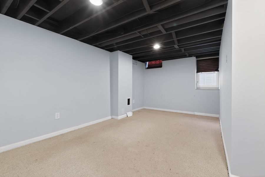 Spacious basement rec room with light gray walls, beige carpet, exposed black ceiling joists, and recessed lighting.