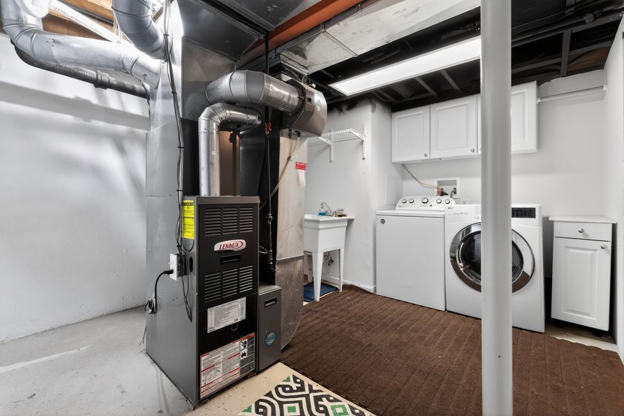 Basement utility room featuring a Lennox furnace, washer and dryer, white cabinets, and exposed ductwork.