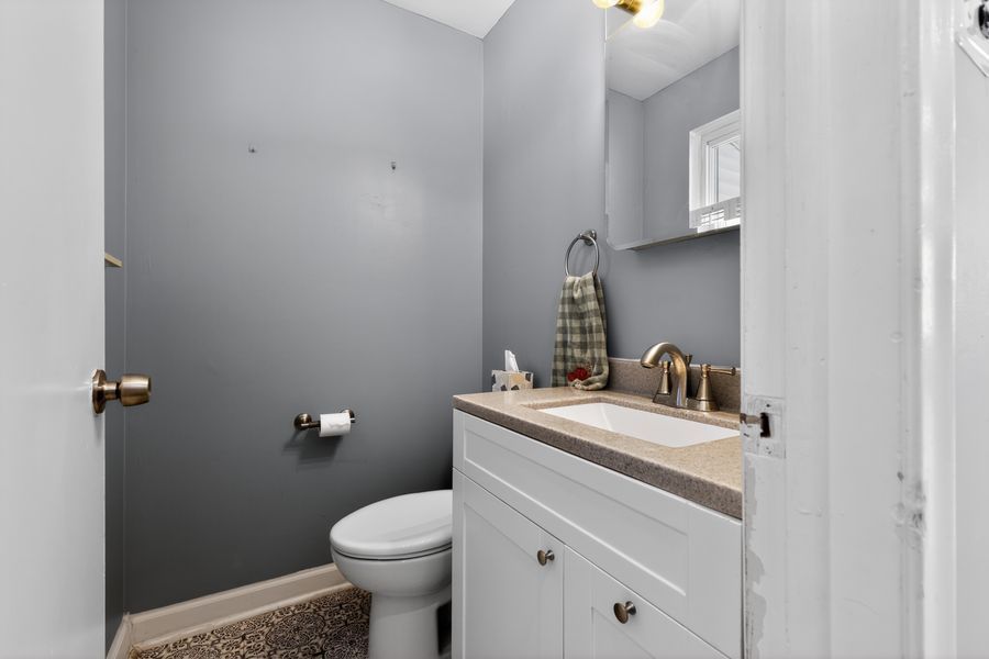 Small half bathroom with white vanity, toilet, gray walls, and a window for natural light.