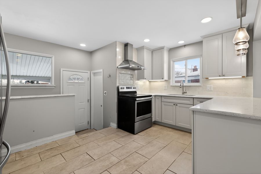 Modern kitchen with gray cabinets, stainless steel appliances, wall-mount range hood, and white quartz countertops.