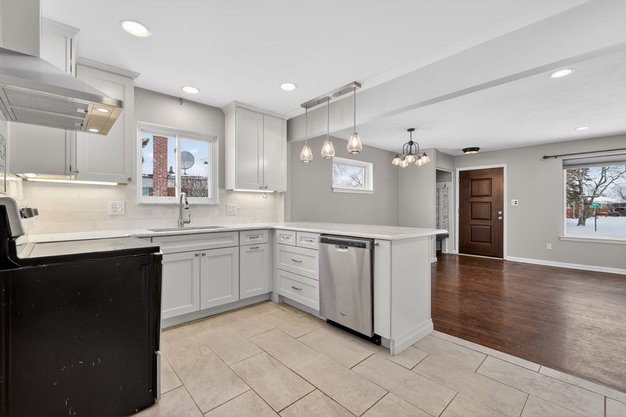 Modern kitchen with gray cabinets, stainless steel dishwasher, pendant lights, and tile flooring opening to hardwood dining area.