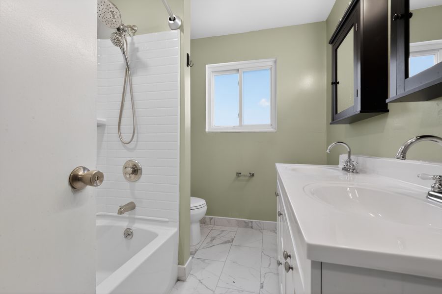 Clean bathroom with tub-shower combo, white vanity, marble tile floors, green walls, and a window for natural light.