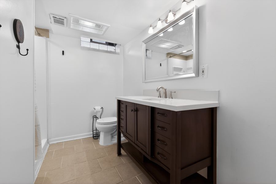 Clean basement bathroom with dark wood vanity, white quartz countertop, large mirror, and tile flooring.
