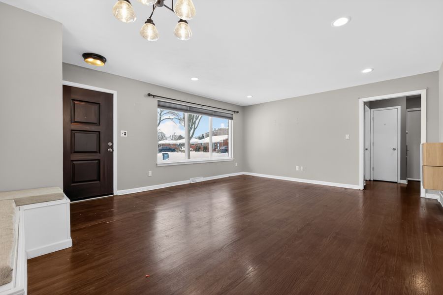 Bright open living room with dark hardwood floors, gray walls, recessed lighting, and a large window with natural light.