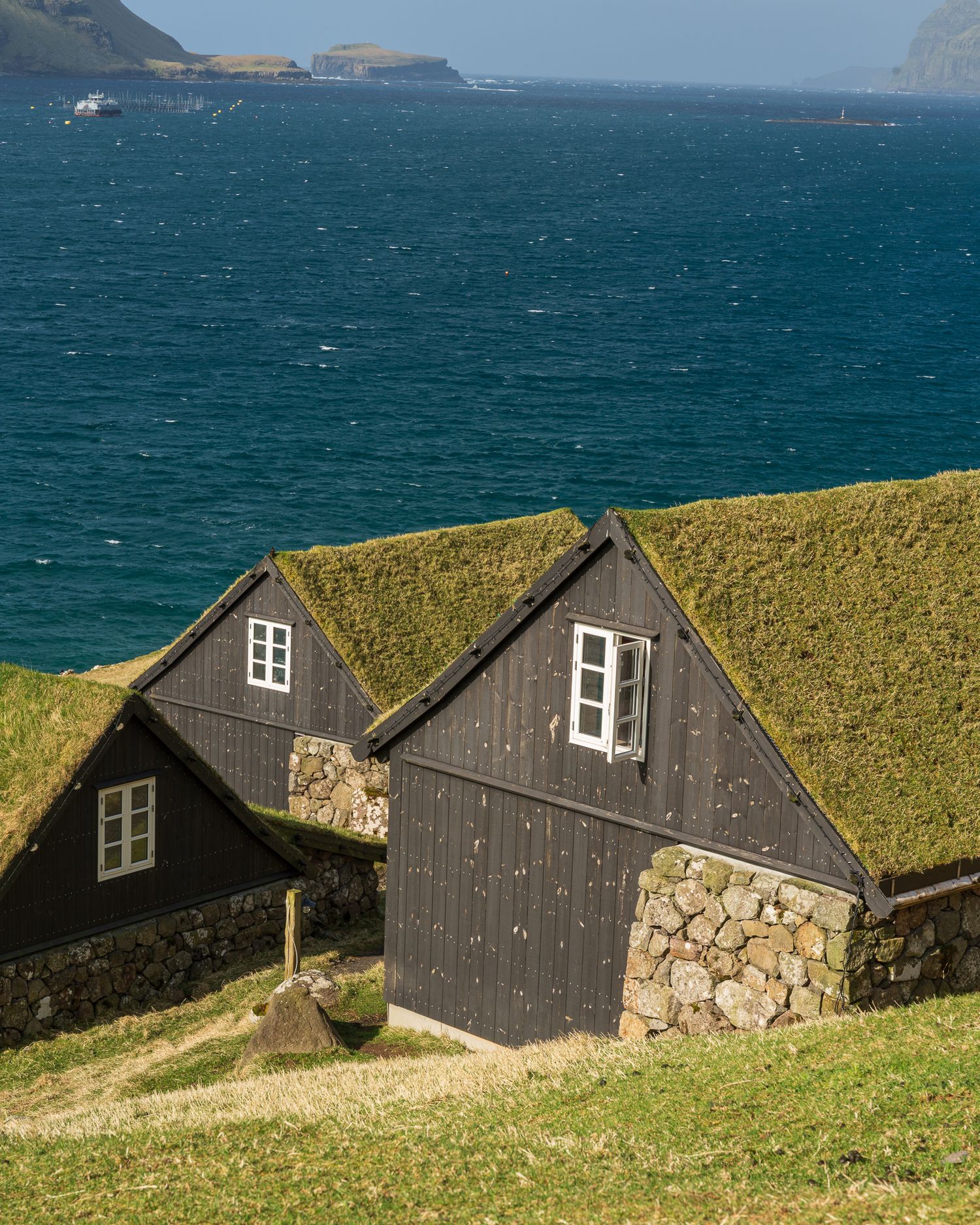 Traditional Faroese turf-roofed black wooden houses overlooking turquoise ocean waters.