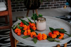 Orange marigold garland surrounding a white candle jar on a round table for a festive Dia de los Muertos display.