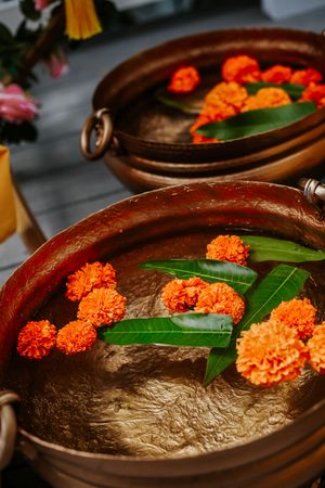 Copper bowls filled with water, orange marigold flowers, and green leaves for a traditional Indian wedding ceremony.