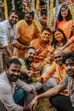 Group of joyful guests in orange attire celebrating at a vibrant Indian Haldi wedding ceremony outdoors.