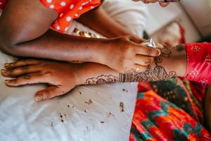 Artist applying intricate henna mehndi design on a woman's hand and wrist in traditional Indian style.