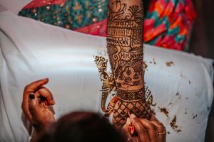 Intricate henna mehndi design being applied on a bride's arm during a traditional South Asian wedding ceremony.