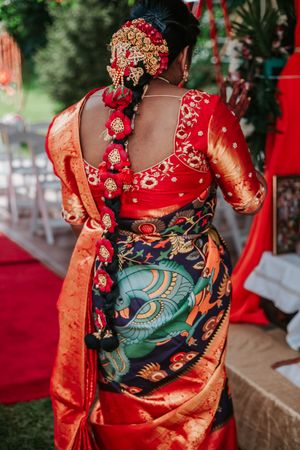 Bride in red embroidered blouse and vibrant Kalamkari saree with floral hair accessories at an Indian wedding.