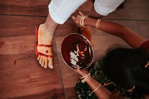Woman applying red alta dye to feet during traditional Indian wedding ritual ceremony on wooden floor.