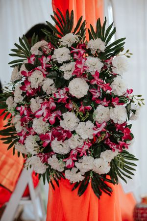 Elegant wedding floral arrangement featuring white carnations and pink orchids with tropical green leaves.
