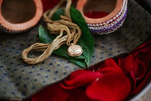 Traditional Indian wedding accessories including gold thali necklace, bangles, and red rose petals on fabric.