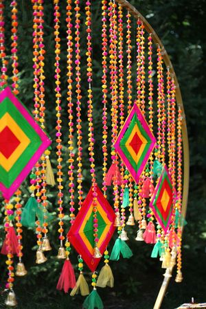 Colorful Indian decorative hanging beads with diamond-shaped ornaments, tassels, and bells in vibrant pink, green, and yellow hues.