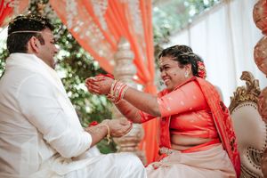 Bride and groom exchanging vows in traditional Indian wedding ceremony with orange decor.