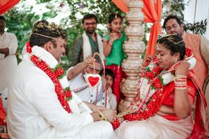 Bride and groom exchange garlands during a traditional Indian Hindu wedding ceremony under a decorated mandap.
