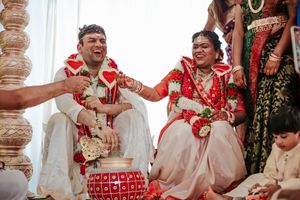 Joyful Hindu wedding ceremony with bride and groom in traditional red and white attire, laughing together during rituals.