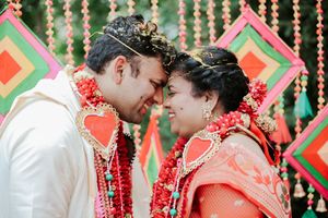 Indian bride and groom sharing a romantic moment wearing red floral garlands at a colorful traditional wedding ceremony.