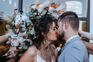 Bride and groom sharing a kiss with large boho bouquet of pampas grass and white flowers.