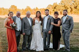 Wedding family portrait on golden autumn field with bride in lace gown and groom in gray suit.