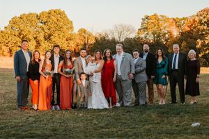 Large family group portrait outdoors during autumn fall wedding celebration with colorful foliage backdrop.