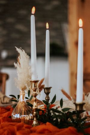 Elegant fall wedding tablescape with lit taper candles, brass holders, pampas grass, and burnt orange linen.