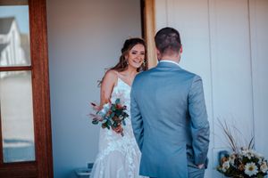 Bride in lace wedding gown smiling at groom during first look moment at barn venue doorway.