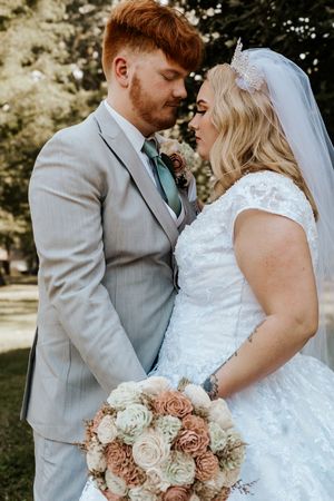 A bride and groom share a romantic moment outdoors, with the bride holding a bouquet of blush and cream roses.