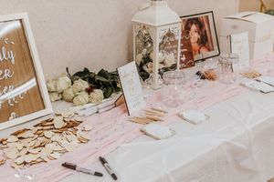 Elegant wedding guest book table with pink runner, white roses, wooden hearts, framed photo, and lantern centerpiece.
