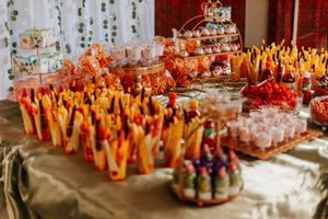 Colorful candy buffet table with orange and red treats, tiered dessert stands, and festive party snacks at a celebration event.