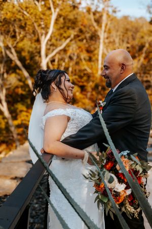 Bride and groom share a romantic moment on a bridge surrounded by vibrant autumn foliage, bride holding a fall bouquet.