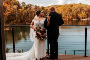 A bride and groom share a romantic moment on a deck overlooking a stunning fall foliage lake view.