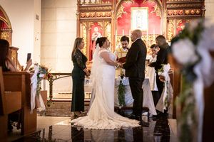 Bride and groom exchange vows at ornate church altar with wedding party and guests during ceremony.