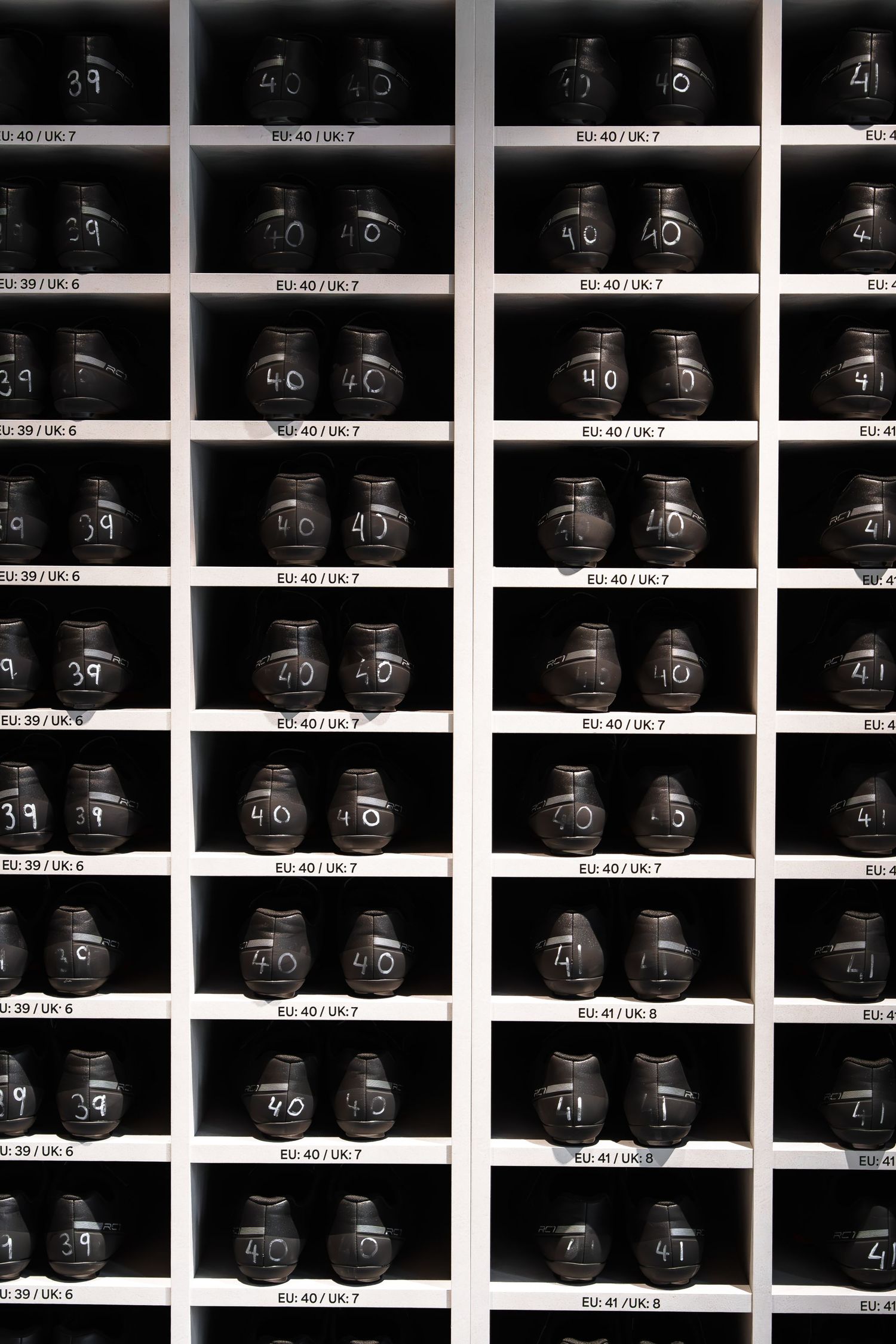 White shelving unit displaying rows of dark bowling shoes labeled with EU and UK sizes.