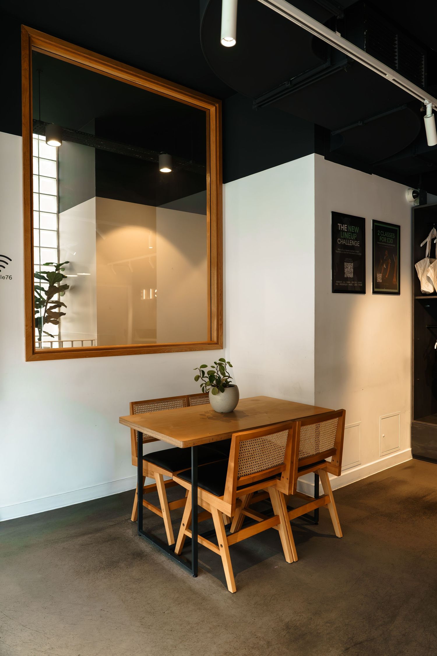 Cozy cafe corner with wooden table, two chairs, large mirror, and small plant on concrete floor.