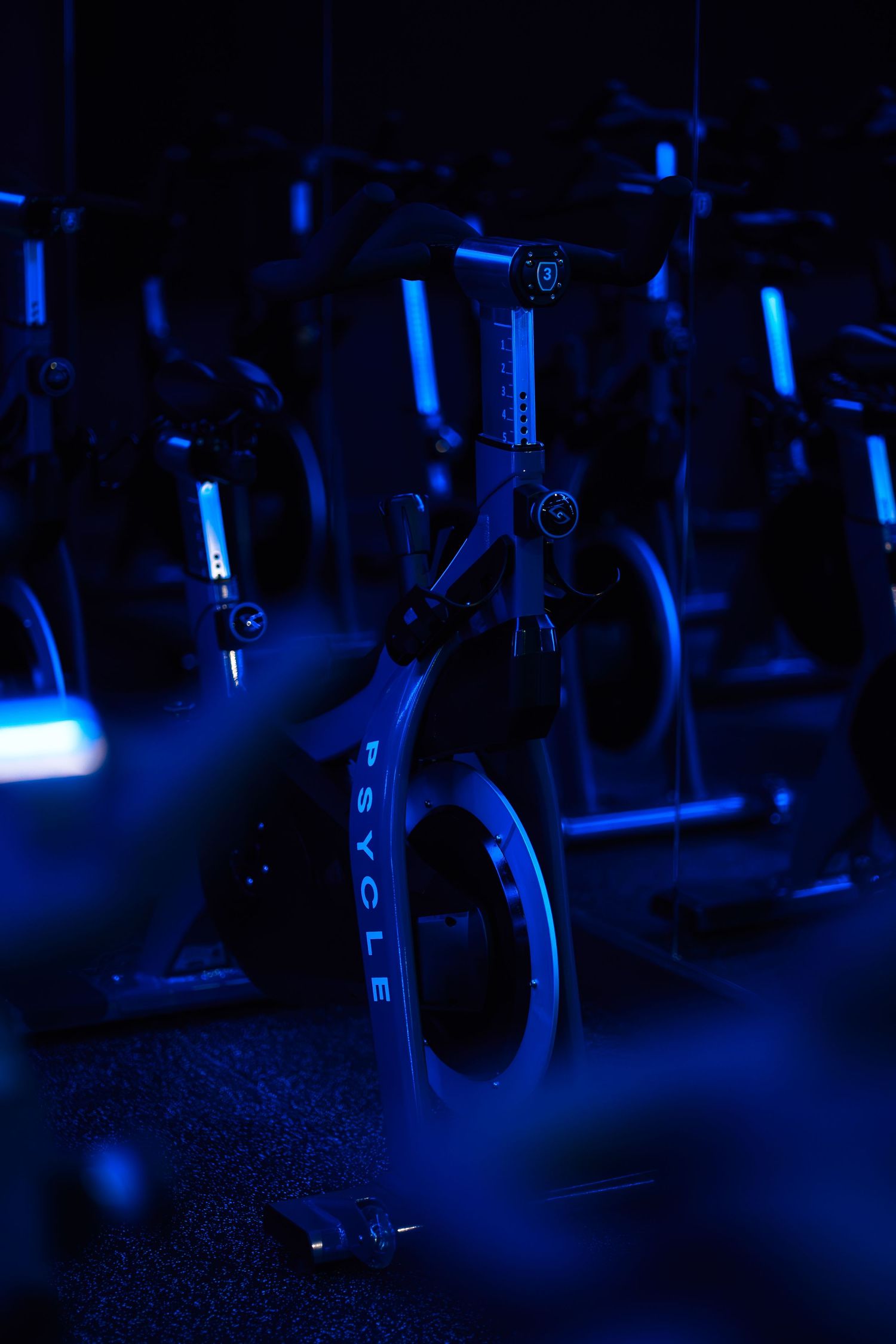 Psycle spin bikes in a dark studio illuminated by dramatic blue neon lighting.