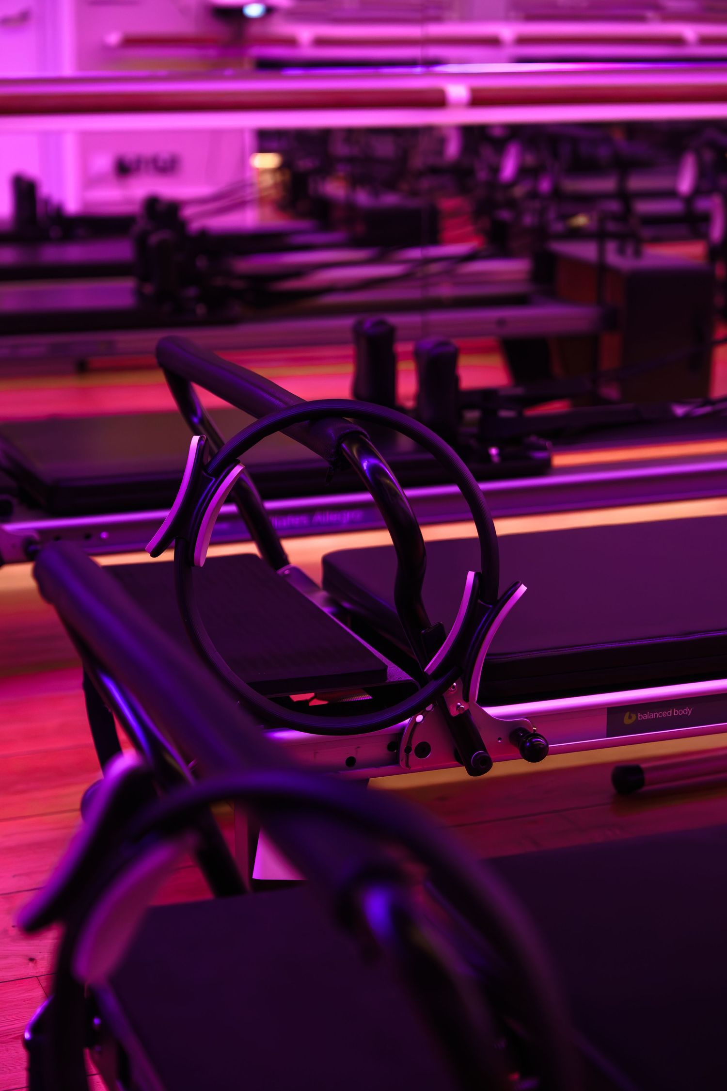Pilates reformer machines in a moody studio with purple and pink ambient lighting.