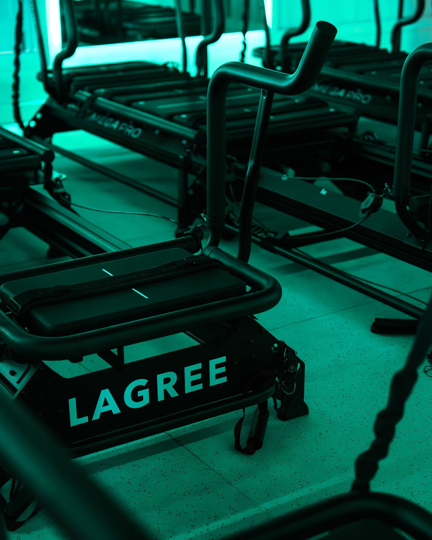 Lagree fitness machines lined up in a dimly lit studio with green ambient lighting, showcasing modern exercise equipment.
