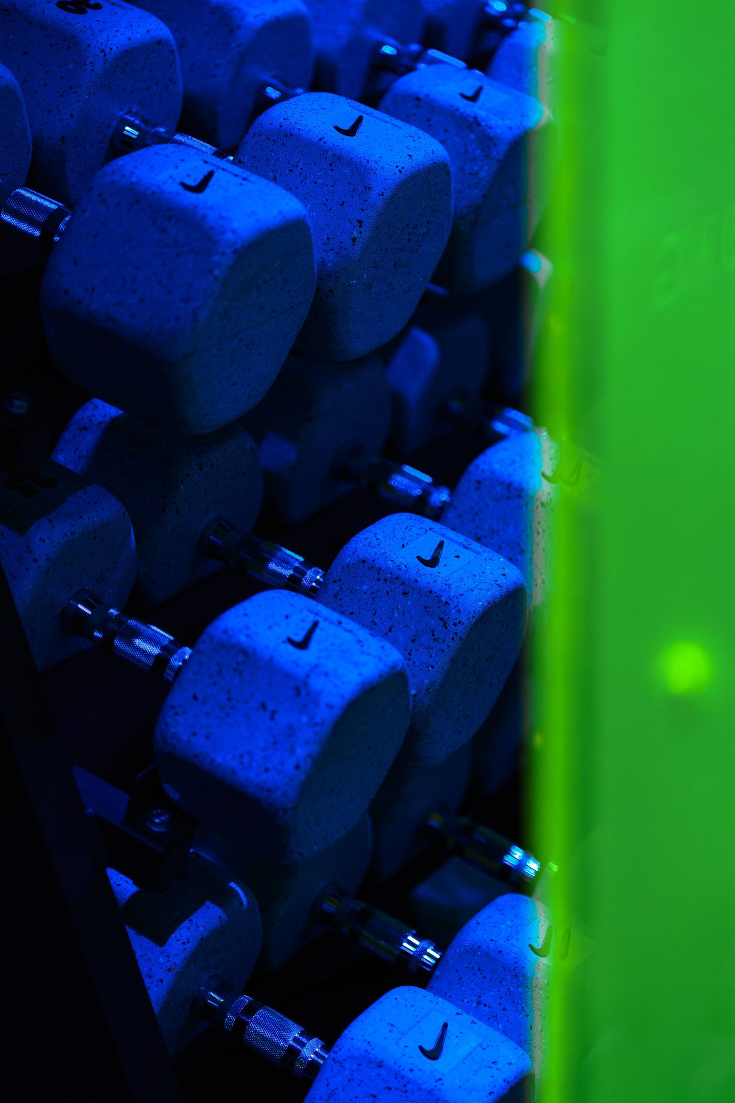 Nike dumbbells arranged on a rack bathed in blue and green neon lighting in a modern gym.